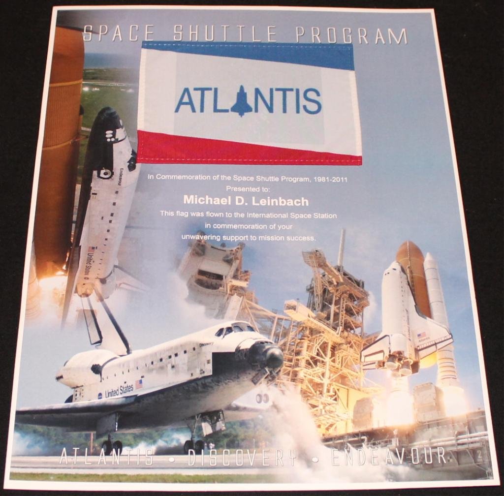 Mike Leinbach's Flown STS-133 Flag: A 4"x 6" Atlantis orbiter flag flown into space aboard Discovery on its STS-133 mission, and it is attached to an 11"x 14" color certificate. The STS-133 flight carried all three orbiter flags, and th