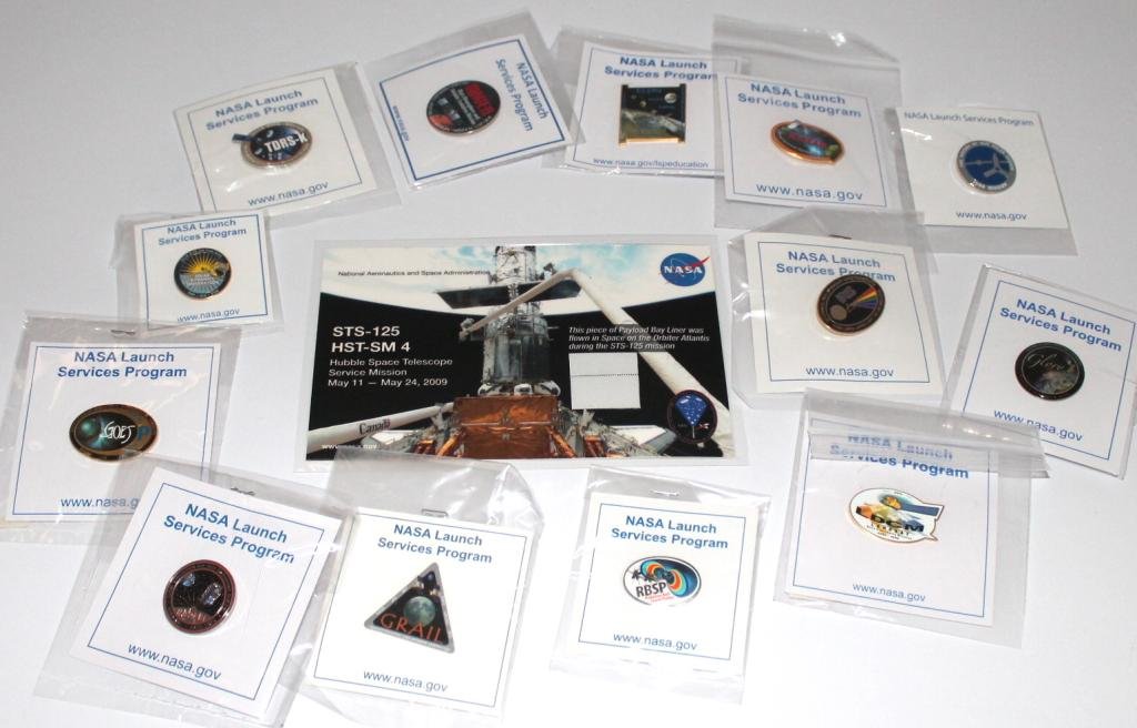 STS-125 Flown Swatch Card and Many Pins: A laminated card bearing a piece of fabric flown on the STS-125 mission, along with many Cape Canaveral side Launch Services lapel pins. Great condition.