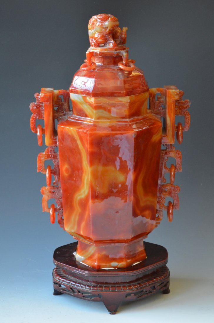 Chinese Carved Carnelian Agate Lidded Vase & Base: Chinese Carved Carnelian Agate Lidded Vase with a seated Foo Lion on the Lid and a wood base. H: 15 Inches Tall