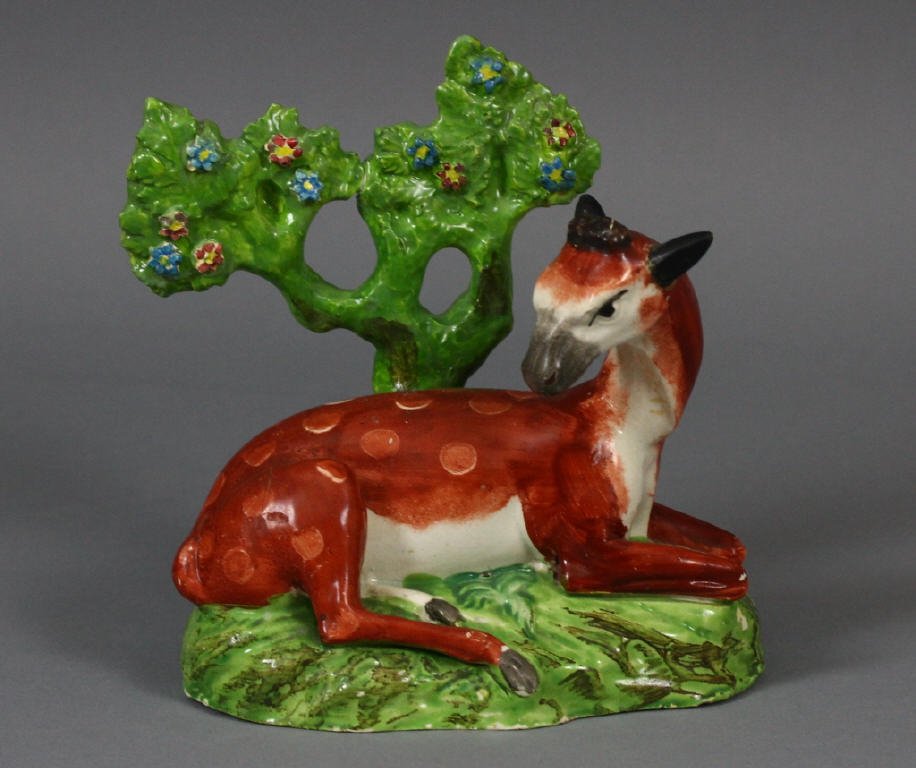 Staffordshire Recumbent Deer with Bocage c.1820: Pre-Victorian, circa 1820 Staffordshire Pearlware figure modeled as a deer lying on a naturalistic oval base before flowering bocage. Decorated . Measures 6'' x 6''.