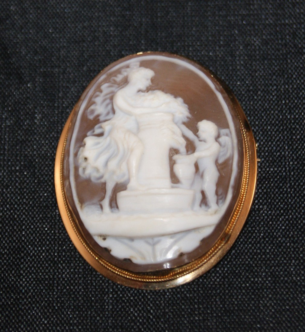 Artisan Carved Oval Shell & 750 Gold Cameo Brooch: Woman on pedestal and angel with urn design in 750 gold bezel. Bezel provides option to be either a brooch or pendant. Total weight of pendant: 7.49g. Measures approx: 1.625" tall x 1.25" wide