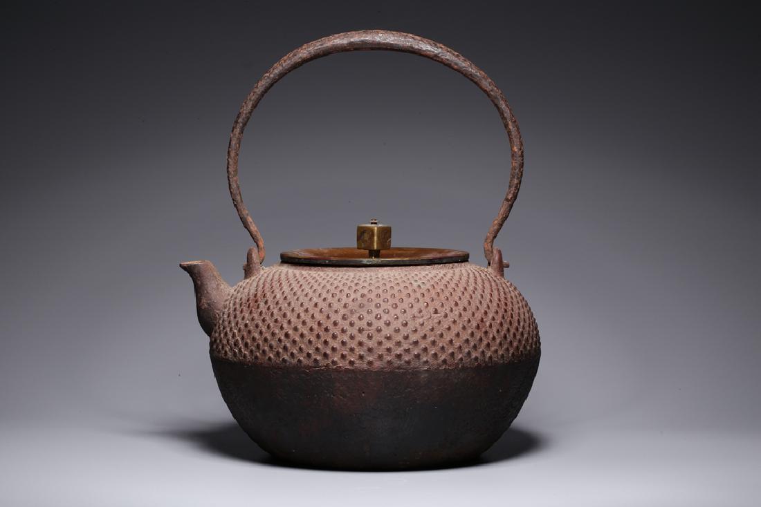 A JANPANESS TETSUBIN IRON TEAPOT, SHOWA PERIOD: Of typical form with short spout, hammered body and tall handle, the cover with finial in the form of a rectangle.22.5 x 19.2 x 17.5 cm