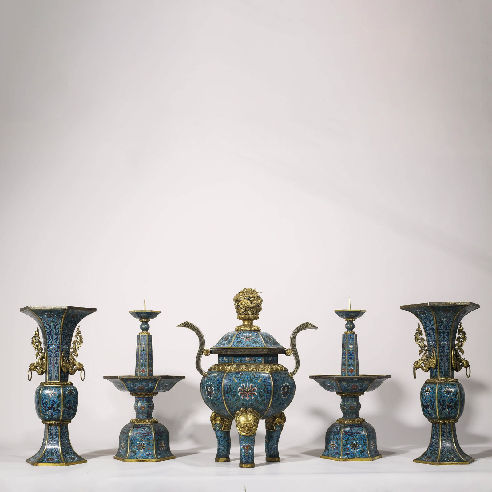 A SET OF CHINESE CLOISONNE ENAMEL ALTAR GARNITURE: Comprising a covered censer in the shape of an archaistic fangding, a pair of pricket candlesticks and a pair of fanggu vases, each decorated with scrolling lotus and foliage between borders of palmet