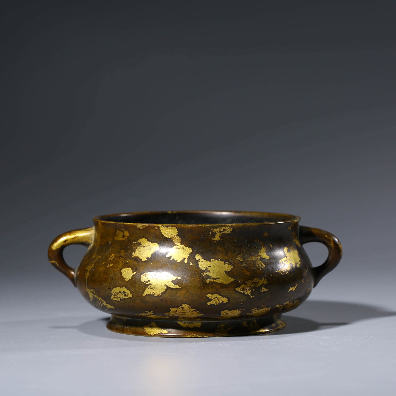 A CHINESE GILT-BRONZE GOLD SPLASHED CENSER: The censer is heavily cast with a compressed globular body inscribed to one side, flanked by twin handles and supported on a ring foot. Weight:721g, Length:5.8cm, Width:13.4cm, Height:6.2cm,