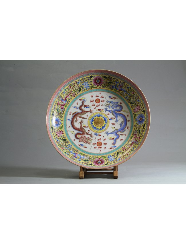 Famille Rose Enamel Plate: Famille Rose enamel plate centered by a Shou emblem surrounded by five blue bats on yellow background. A blue and copper colored five clawed dragon face one another surrounded by stylized flames and c