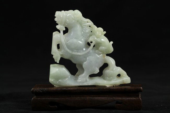 An intricately carved white jadeite horse: An intricately carved white jadeite horse, with front hoof raised high, a monkey riding on its back and holding to mane, with wooden base, of excellent detailing. Length 4.6" Width 1.6" Height 4.2"