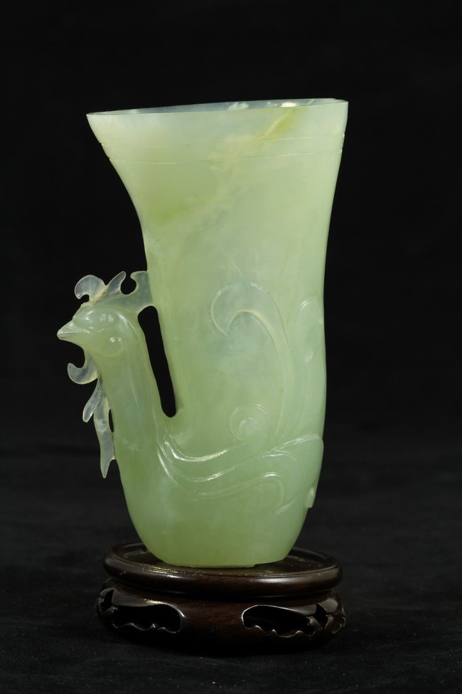 A carved jade of horn shaped phoenix: A carved jade of horn shaped phoenix, with yellow hue, of intricate detailing on crest and feather, with wooden base. Diameter 3" Height 5.5"