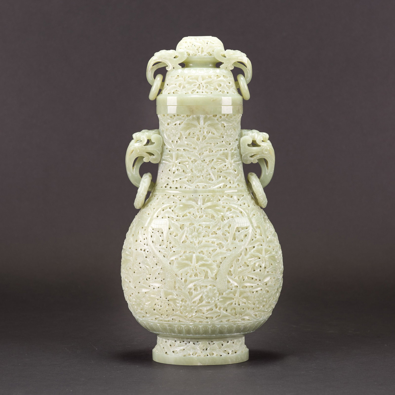 A CARVED CELADON WHITE JADE VASE AND COVER, MID-20TH CENTURY: A carved celadon white jade vase and cover, the vase is carved on the body in open work design of flowers and phoenix, the shoulder and neck are flanked by a pair of elephant, the cover is similarly.H