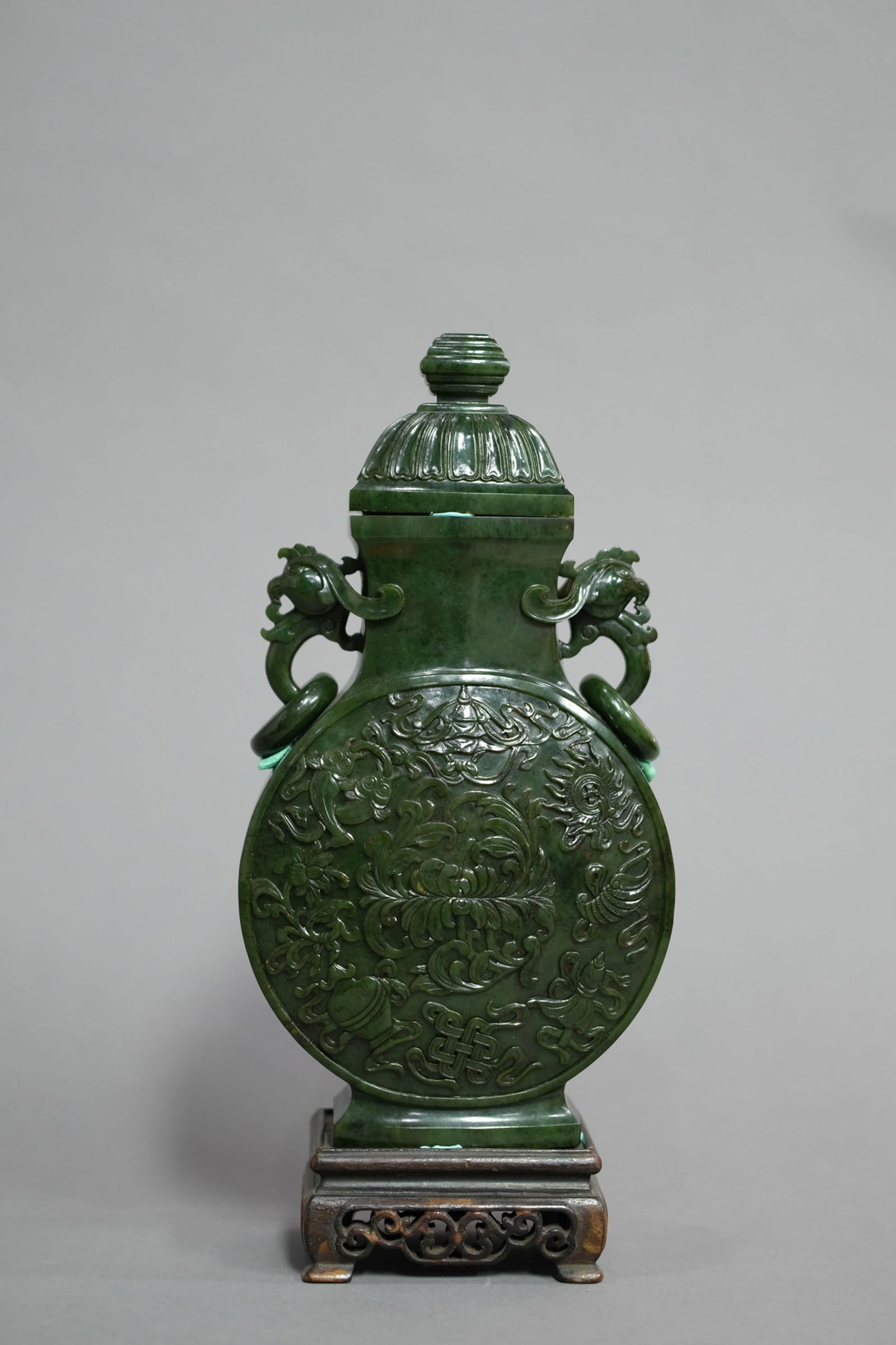 SPINACH GREEN JADE DOUBLE-EARED OBLATE VASE: Spinach green jade double-eared oblate vase. Dimensions: With stand Height: 31 cm, Vase Height: 27 cm.