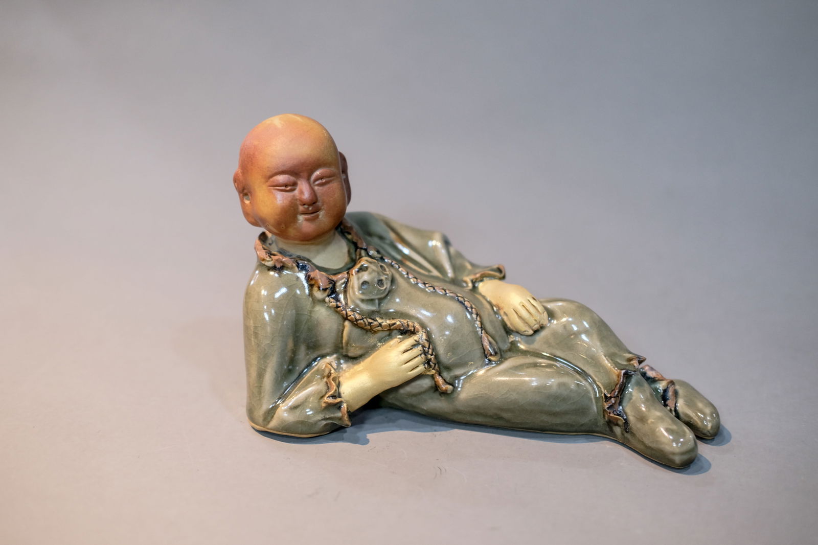 CELADON GLAZE MONK FIGURINE: Celadon glaze monk figurine.Dimensions: Length: 19.5 cm, Height: 12 cm.