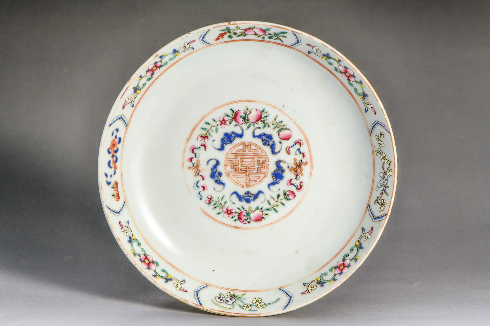 A FAMILLE ROSE 'FIVE BATS HOLDING A SHOU' DISH: A famille rose 'five bats holding a shou' dish.Dimensions: Diameter: 17.5 cm (6.89 in.), Height: 3 cm (1.18 in.). All measurements are approximate.