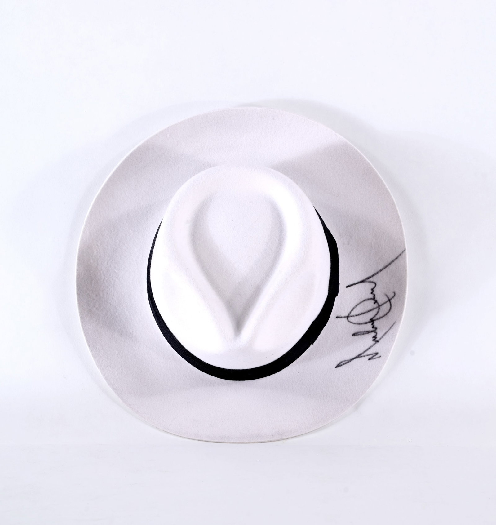 FEDORA HAT BEARING SIGNATURE ATTRIBUTED TO MICHAEL JACKSON: The hat features a classic fedora form in a light tone with a contrasting dark band encircling the crown. A mark is clearly visible along the brim, exhibiting fluid pen strokes. The condition shows li