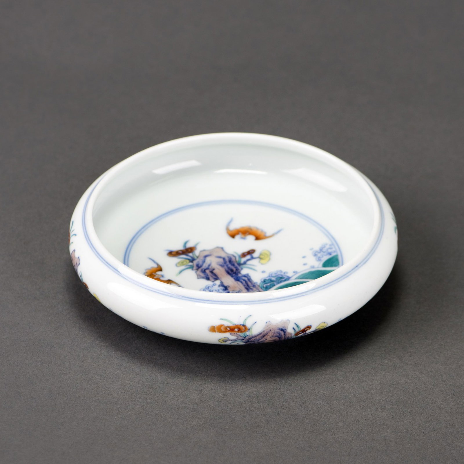 CHINESE DOUCAI PORCELAIN BRUSH WASHER, QIANLONG MARK: Chinese doucai porcelain brush washer with a compressed low body raised on a short foot, featuring polychrome decoration of phoenixes hovering above waves crashing against rocks on the interior and ex