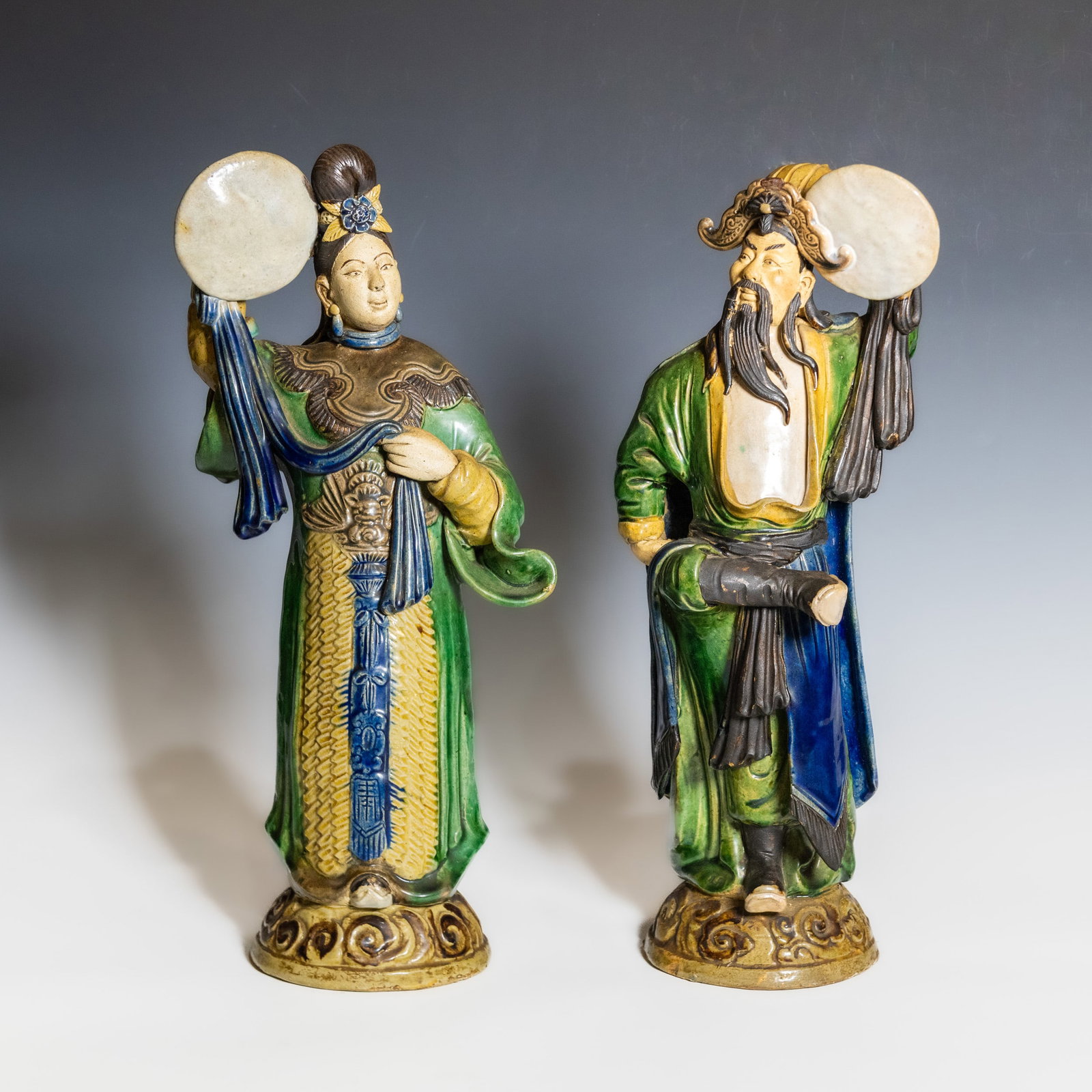 (LOT OF 2) A PAIR OF CHINESE SHIWAN POTTERY FIGURES: (lot of 2) A pair of Chinese Shiwan-style pottery figures, depicting a standing gentleman and lady, each holding a circular fan and dressed in flowing robes decorated with green, blue, cream, and brow