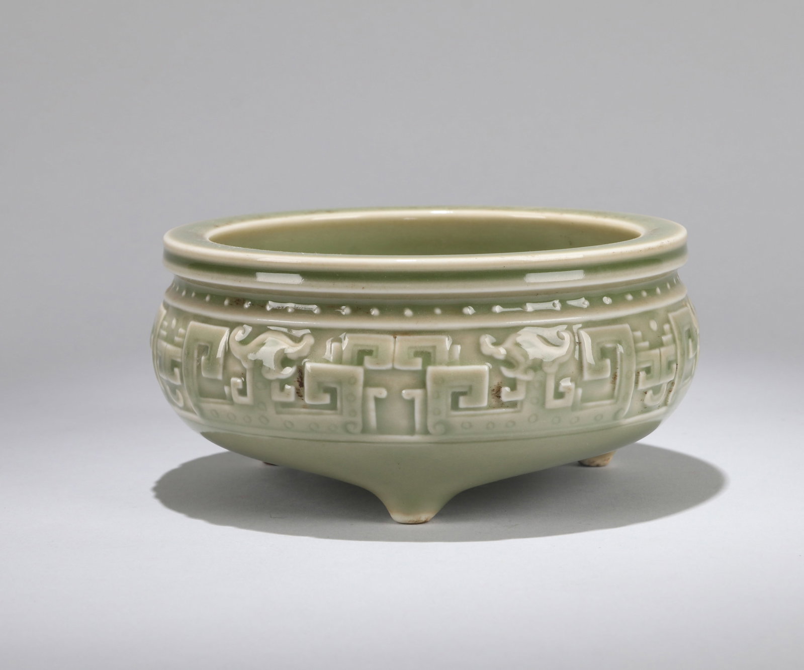 A CELADON-GLAZED MOLDED 'ARCHAISTIC DRAGON' TRIPOD CENSER