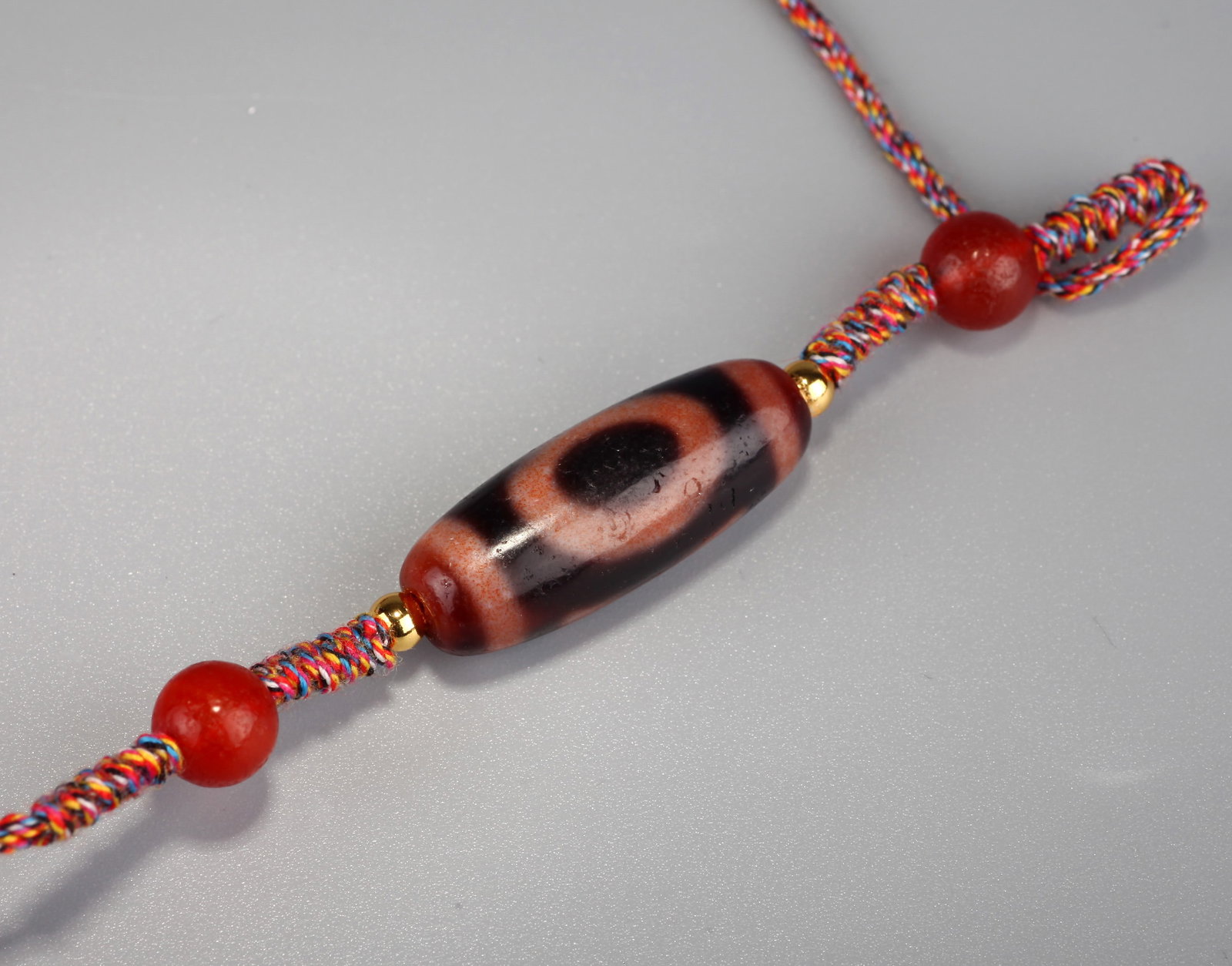 A CINNABAR-COLORED DZI-STYLE BEAD