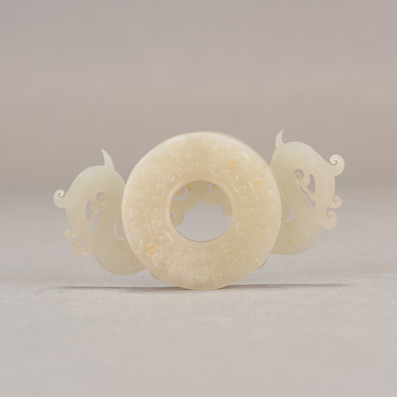 A CHINESE ARCHAISTIC PALE CELADON JADE BI-FORM ORNAMENT: A Chinese archaistic pale celadon jade bi-form ornament. 2.24"h x 4.06"w x 0.39"l (5.7 x 10.3 x 1 cm)
