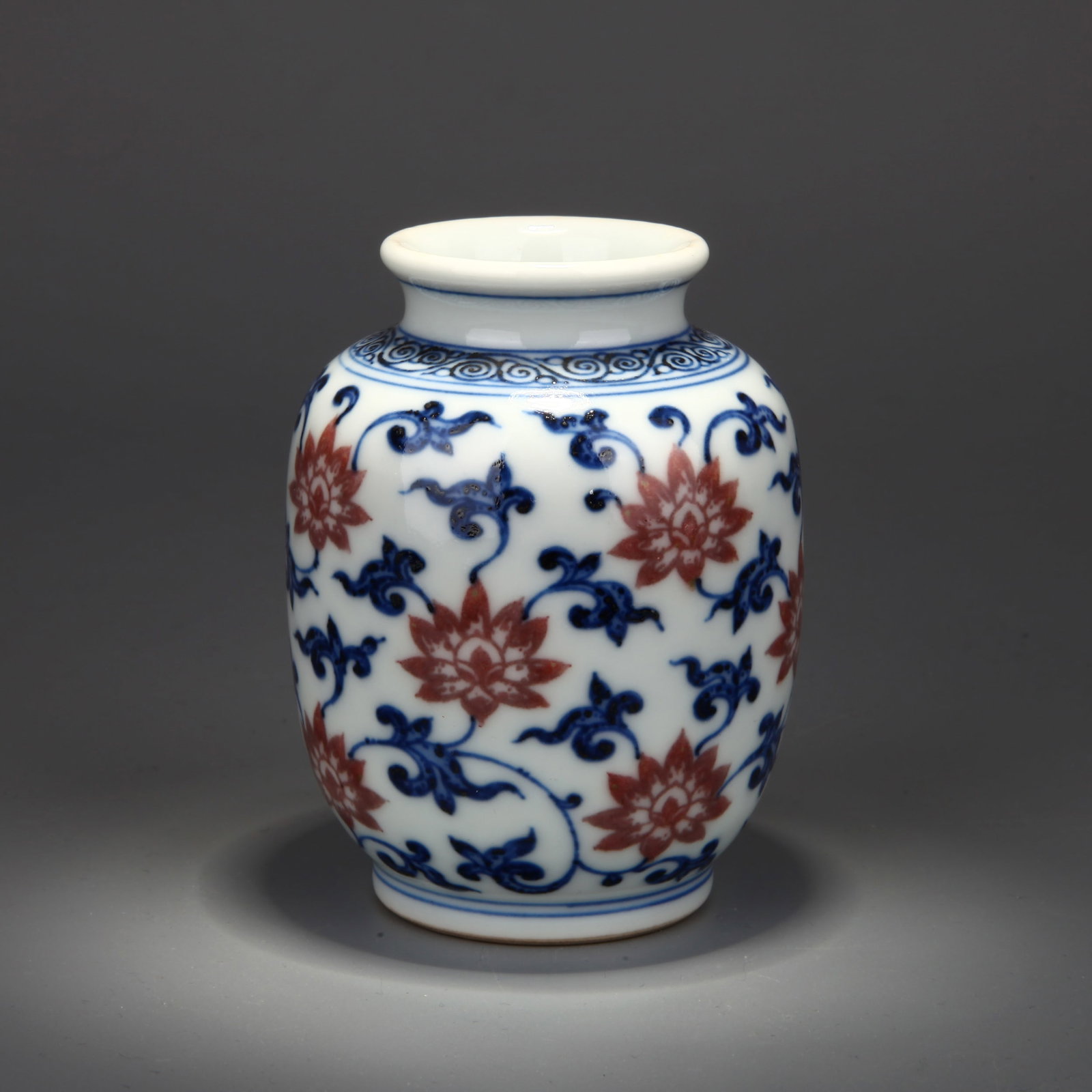 A BLUE-AND-WHITE AND UNDERGLAZE-RED 'FLORAL SCROLL' SMALL JAR: A blue-and-white and underglaze-red small jar decorated with floral scrolls. Height 9 cm, diameter 6.8 cm.