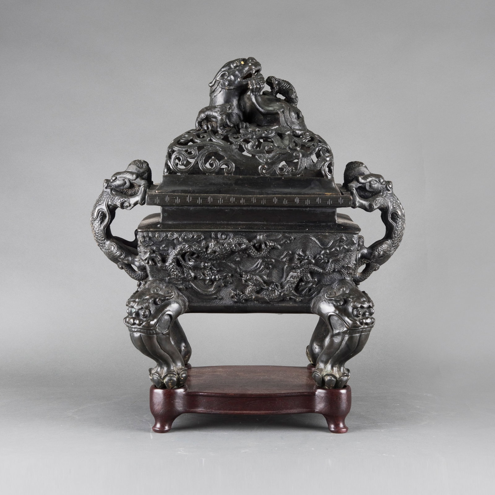 A CHINESE BRONZE CENSER WITH LION FINIAL, 19TH CENTURY: A Chinese bronze censer, 19th century, of square form, decorated in relief with dragons and flanked by a pair of handles, raised on four beast-form feet. The openwork cover is surmounted by a lion fin