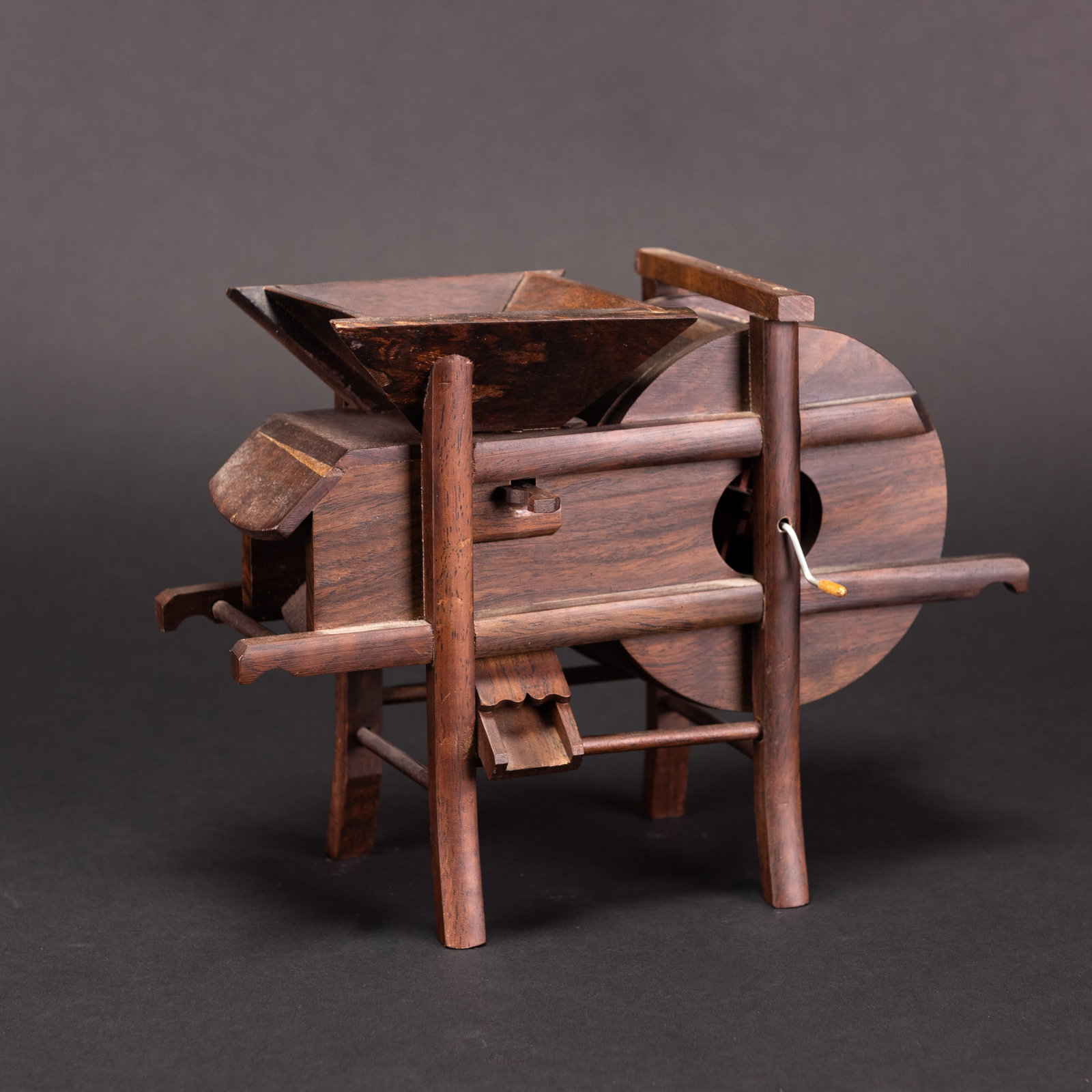 A WOODEN MODEL OF AN AGRICULTURAL TOOL: A wooden model of an agricultural tool, raised on four supports and fitted with a hopper and a large wheel. 9.75"l x 3.5"w x 7"h