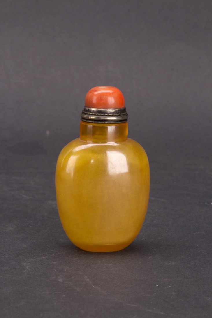 Chinese Peking Glass Snuff Bottle: Peking Glass snuff bottle in a luminous marigold shade of compressed ovoid form with semi-precious stone cap and metallic rim detailing. Height 3.25"