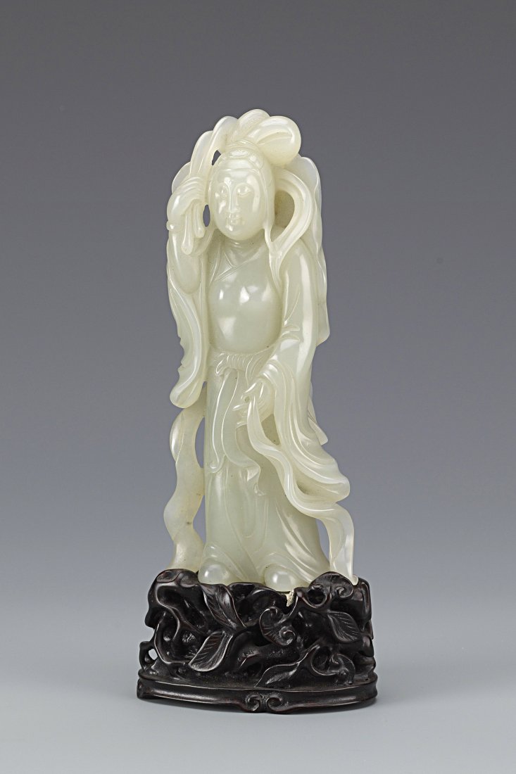 A Chinese Nephrite White Jade Figure of Guanyin: A Chinese Nephrite White Jade Figure of Guanyin, standing wearing a long-sleeved flowing robe, holding a branch leaf in the right hand and a ribbon in the left, the face with serene expression, suppor