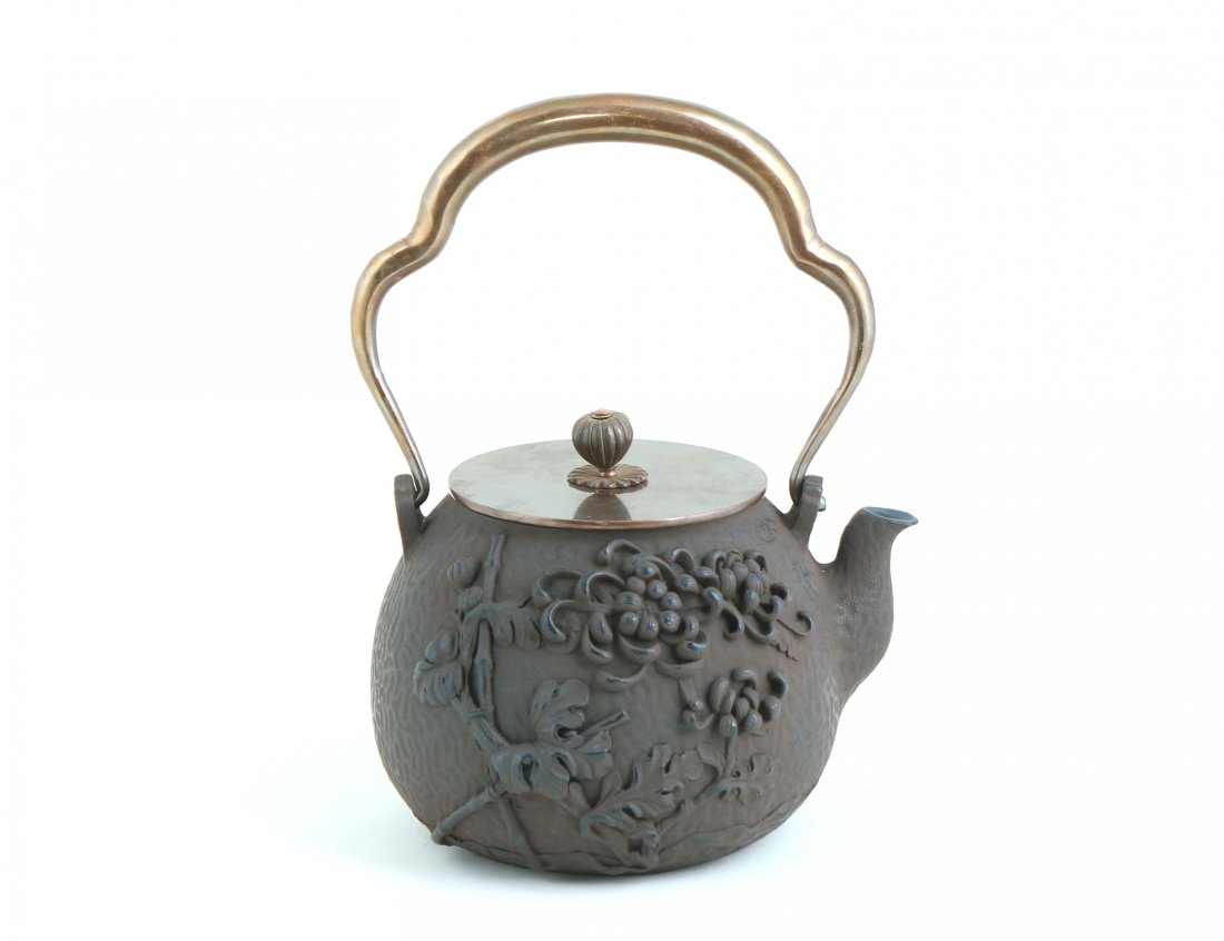 A Japanese style Iron Teapot: A floral relief on one side and grass relief on the other. The handle and lid are made of silver-copper alloy. Engraved on underside of lid. Length 6.5" Width 6.5" Height 9"