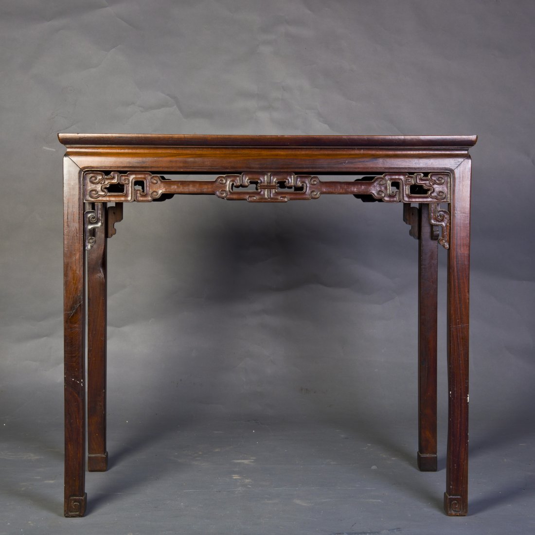 A HARDWOOD RECTANGULAR TABLE: The single board top set into a mitered, mortise and tenon frame over a waisted and reticulated apron of stretched scrolling clouds, joined to legs ending in scrolling clouds. Length 37" Width 18" Hei