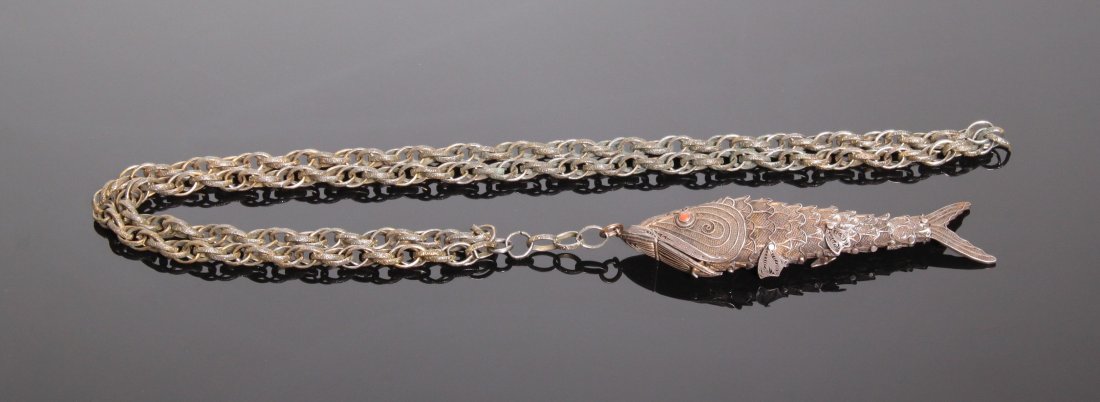 Vintage pill box necklace in the form of a fish with a: Vintage pill box necklace in the form of a fish with a segmented and articulated body with moving fins. The fishes mouth opens to allow access to the box. There are 2 circular inset cabochons of red c