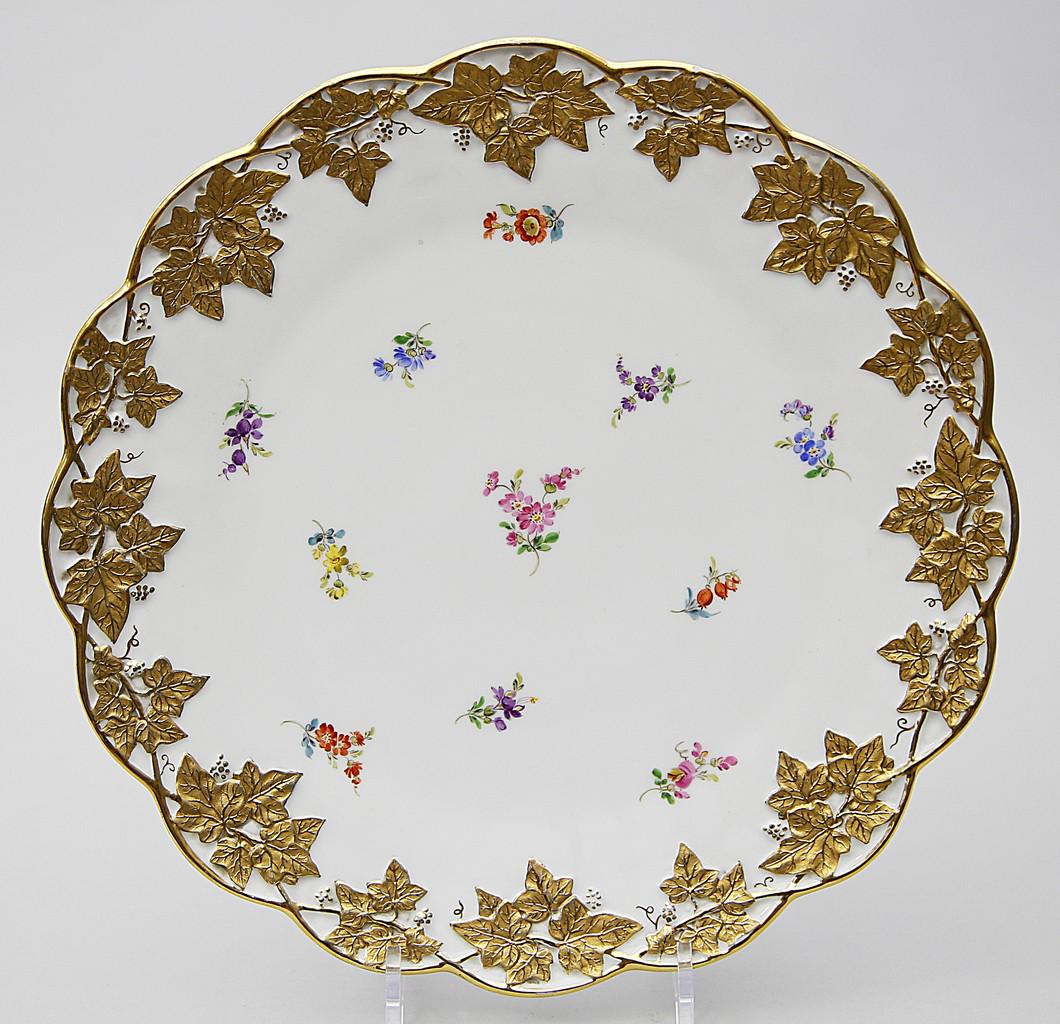 Tortenplatte, Meissen.: Fahne mit Efeurrelief, in Glanz- und Mattgold abgesetzt. Bunte, gestreute Blumenmalerei. Schwertermarke Meissen, 1924-1934. 2. Wahl. D. ca. 32,5 cm.