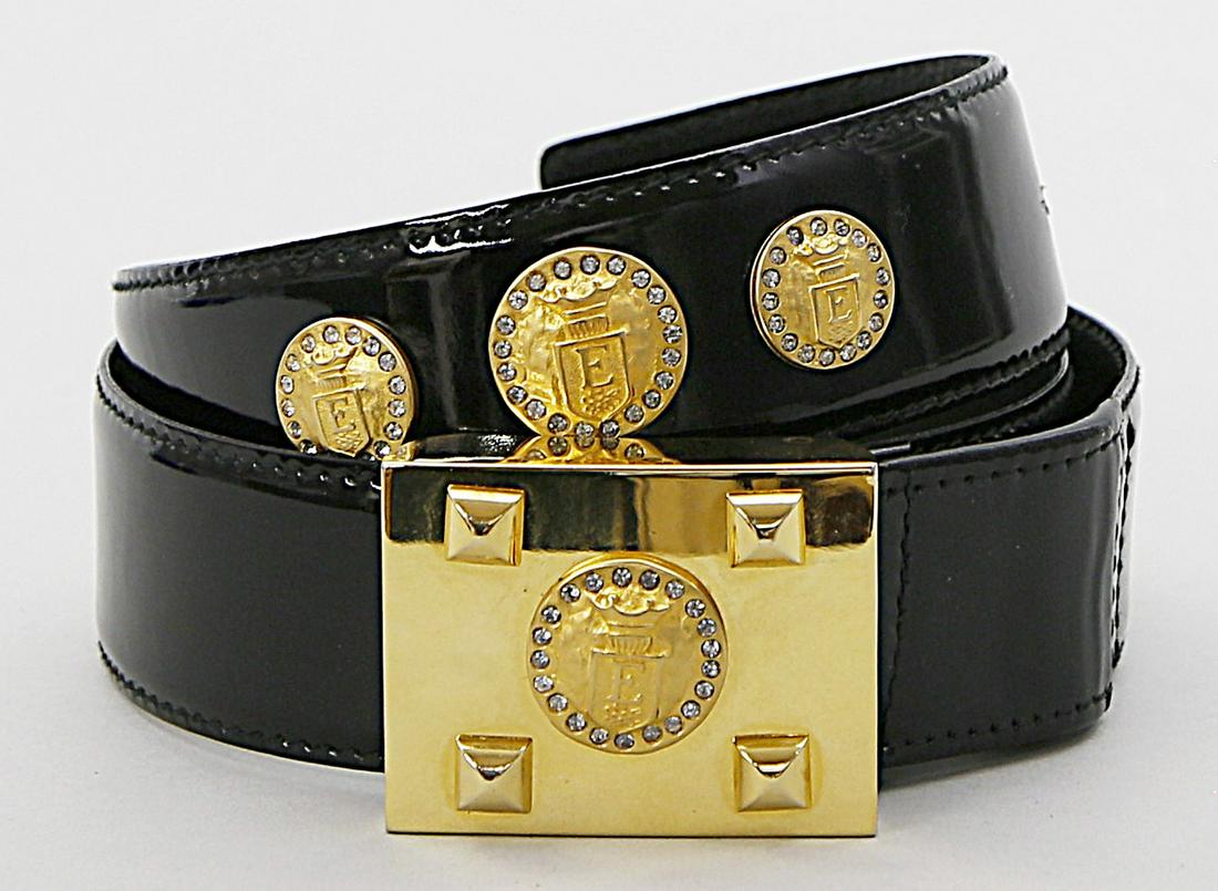 Gürtel, "Escada".: Schwarzes Lackleder. Runde Applikationen mit Escada-Wappen und farblosem Strasssteinbesatz sowie rechteckige Schließe aus vergoldetem Metall. L. Tragespuren. B. 4,5, L. 90 cm (bis zum äu