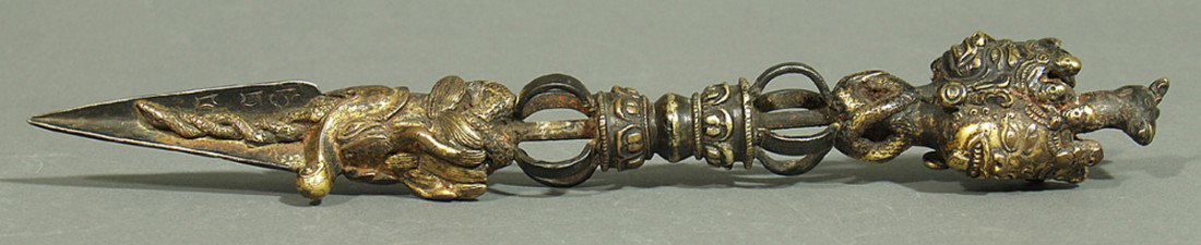 Phurba (Ritualdolch).: Bronze, feuervergoldet und Meteoritenstahl. Teils versilbert. L. berieben. Als Knauf das mit Pferdekopf bekönte Haupt der Schutzgöttin Hayagriva, es zeigt drei Gesichter, zwei davon mit zornigem Aus