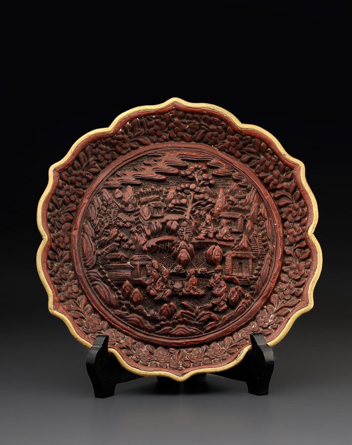 CHINA, 19TH CENTURY: A FINE CINNABAR LACQUER CHARGER MARKED QIANLONG CHINA, CIRCA 1900 The cavetto adorned with immortals (xianren) amidst rocks, pavilions and pine trees, the wide rim with plum tree flowers (meihua), the