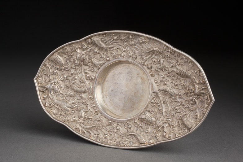 ANTIQUE CHINESE EXPORT SILVER CANDLESTICK-HOLDER-CES: A CHINESE EXPORT SILVER CANDLESTICK HOLDER CHINA, LATE 19TH-EARLY 20TH CENTURY With a scalloped rim, adorned in repoussé with a décor of dragons crawling amidst clouds in pursuance of the flaming pe