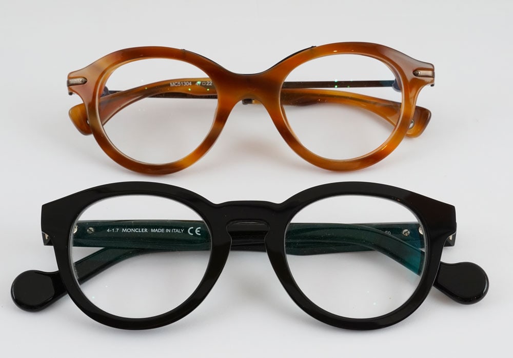 MONCLER -: Description française: MONCLER - Lot de 2 paires de lunettes de vue Moncler, l'une avec une monture noire, l'autre marron. Verres tranparents avec corrections. English Description: MONCLER - Set