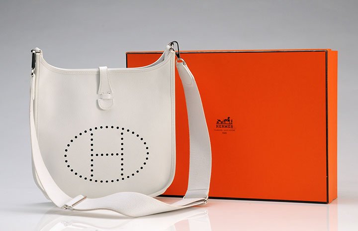 HERMÈS - MADE IN FRANCE: White grained leather ''Evelyne'' decorated with the perforated H on the front, tab on snap fastener, palladium hook, adjustable shoulder strap. With its dust bag and the box. Length: 31cm - 12''