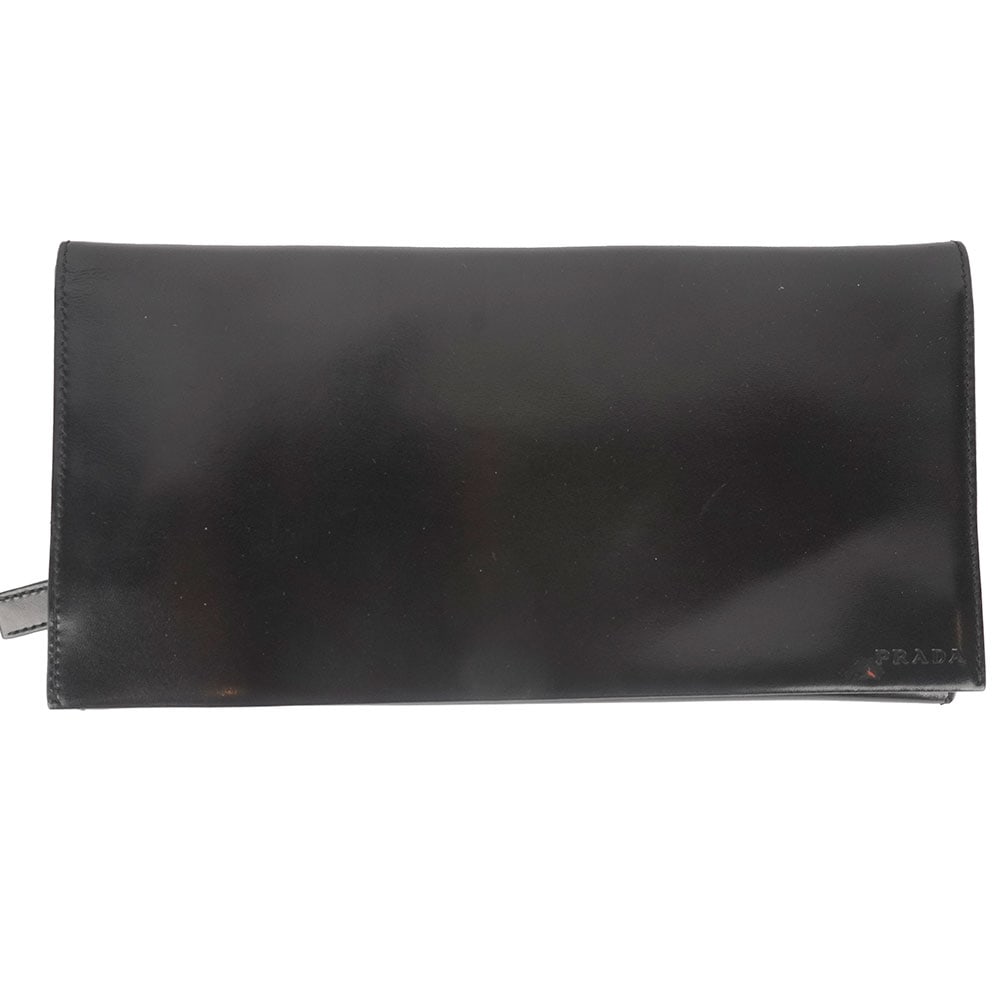 PRADA: Description française: PRADA Pochette de voyage Prada en cuir noir laqué, fermeture par rabat à boutons de pressions, plusieurs compartiments pour des billets d'avion, passeport,