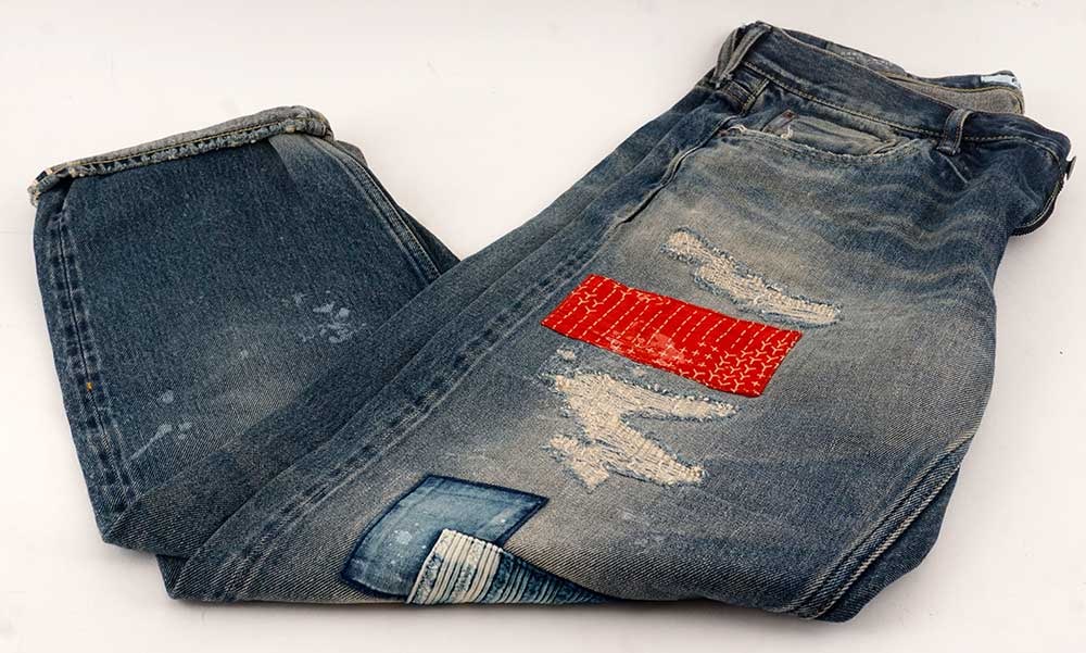 FDMTL: Description française: FDMTL Jeans bleu avec déchirrures et patchowrork bleus et rouges. Taille 34. English Description: FDMTL Distressed blue jeans with red and blue patchwork. Size 34.