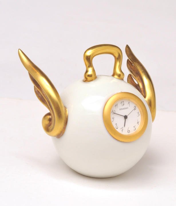 BERNARDAUD: BERNARDAUD A polychrome porcelain traveling clock flanked by angel style wings. H: 9 cm - 3.5''