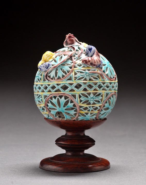 PORCELAIN OPENED-WORK BALLS: Two polychrome porcelain opened-work balls, decorated with rosettes and flowers in relief, on wooden bases. From an important Canadian family. H : 10,5 cm ; 4 inches. L/W : 7 cm ; 2,5 inches.