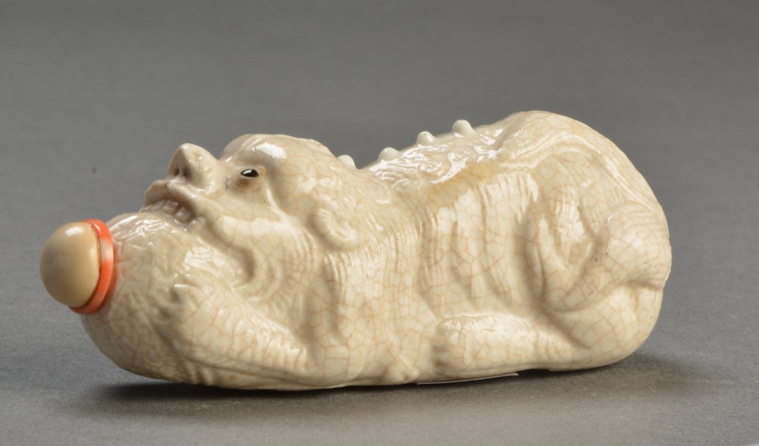 GLAZED SOFT PASTE PORCELAIN SNUFF BOTTLE: GLAZED SOFT PASTE PORCELAIN SNUFF BOTTLE molded in the form of a foo-dog biting a ball, China, QING DYNASTY. Stopper. L: 7,5cm - 3" E : 200 / 300 #57