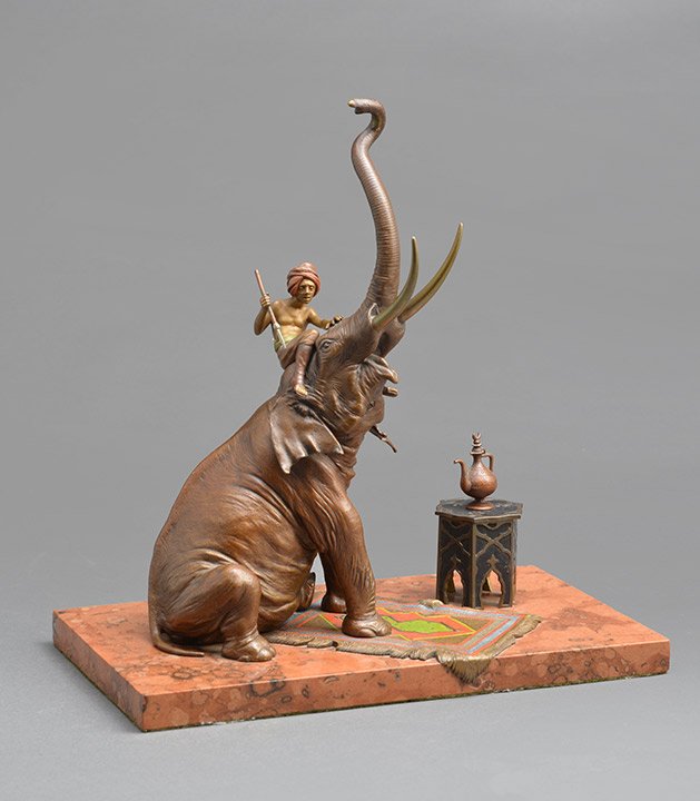 BERGMAN, Franz (1898-1963): BERGMAN, Franz (1898-1963)Polychrome bronze elephant driver and sitting elephant, raised trunk, it rests on a rug, next to it, an hexagonal table and large teapot. Stamped "B" under the table top and 