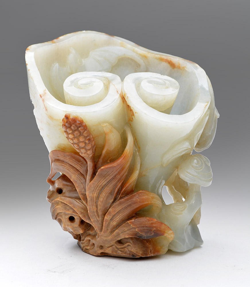 CHINA - JADE: LIGHT CELADON AND BROWN NEPHRITIS LINGZHI SHAPED CUP, CARRYING A BAT AND ON RELIEF OF FLOWERS AND LINGZHI CHINA H. 12cm – 4.75’’ E: 5.000-6.000