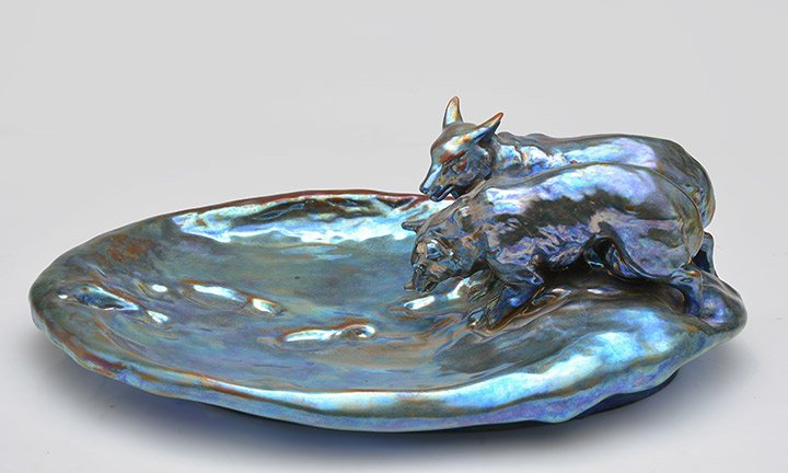 ZSOLNAY-PECS – HONGRIE (1853-) Iridescent enameled: ZSOLNAY-PECS – HONGRIE (1853-) Iridescent enameled ceramic trinket bowl cup with blue, copper, and green shade representing two wolves following footprints. Signed on the reverse on the base with
