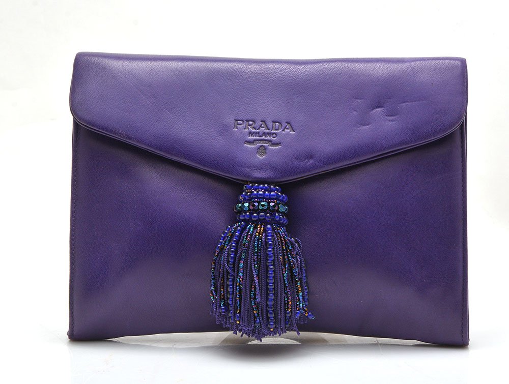 PRADA - MADE IN ITALY: PRADA - MADE IN ITALY purple leather clutch signed on the center and adorned with a pompom, interior with a zipped pocket, magnetic snap closure. H: 17cm - 6.75" L: 23cm - 9"