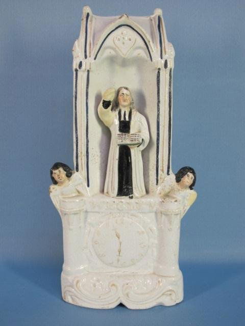 Staffordshire figure of John Wesley: Staffordshire figure of John Wesley standing in the pulpit on a titled gilt lined rococo base with clock face and angels to his side. His right hand is pointing in the air while left hand holds open a