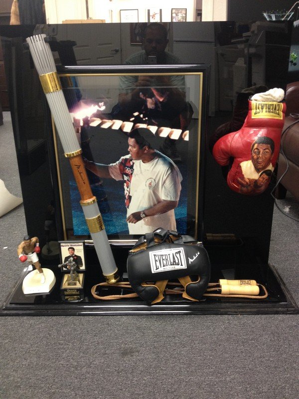 SPORTS MEMORABILIA - A SHRINE TO MUHAMMED ALI - A LARGE: SPORTS MEMORABILIA - A SHRINE TO MUHAMMED ALI - A LARGE LUCITE DISPLAY CASE MEASURING APPROXIMATELY 38''L x 11''W x 36''H - THE CASE CONTAINS: 1996 OLYMPIC TORCH RELAY PHOTO SIGNED MUHAMMED ALI / OLYM