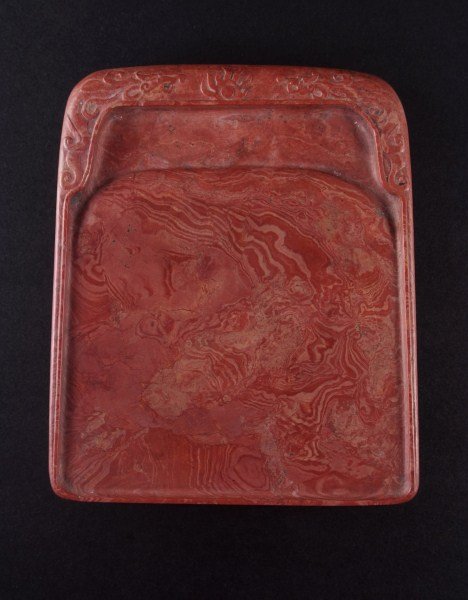 A Red-Vein Inkstone: Of rectangular form, carved with floral sprays on the upper surface, the rare stone of coral-red color suffused with a pattern of sky clouds with veins of white tone. Length:7.25, Width:6, Height:1.25