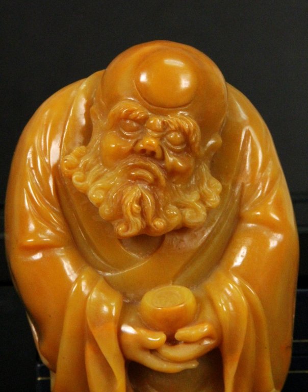 A Carved Yellow Jade of an Old Man: Finely carved in the form of Old man holding a coupe, the stone of brilliant brown-yellow color. Length:4, Width:2.75, Height:2.25