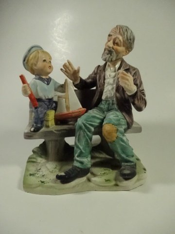PORCELAIN FIGURINE, MAN & BOY ON BENCH WITH TOY: PORCELAIN FIGURINE, MAN & BOY ON BENCH WITH TOY SAILBOAT, APPROX 7.5" X 6.5"